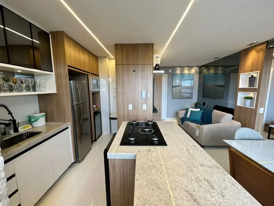 Cozinha com ilha de cooktop, armários e nichos em madeira, iluminação em LED e sala de estar ao fundo