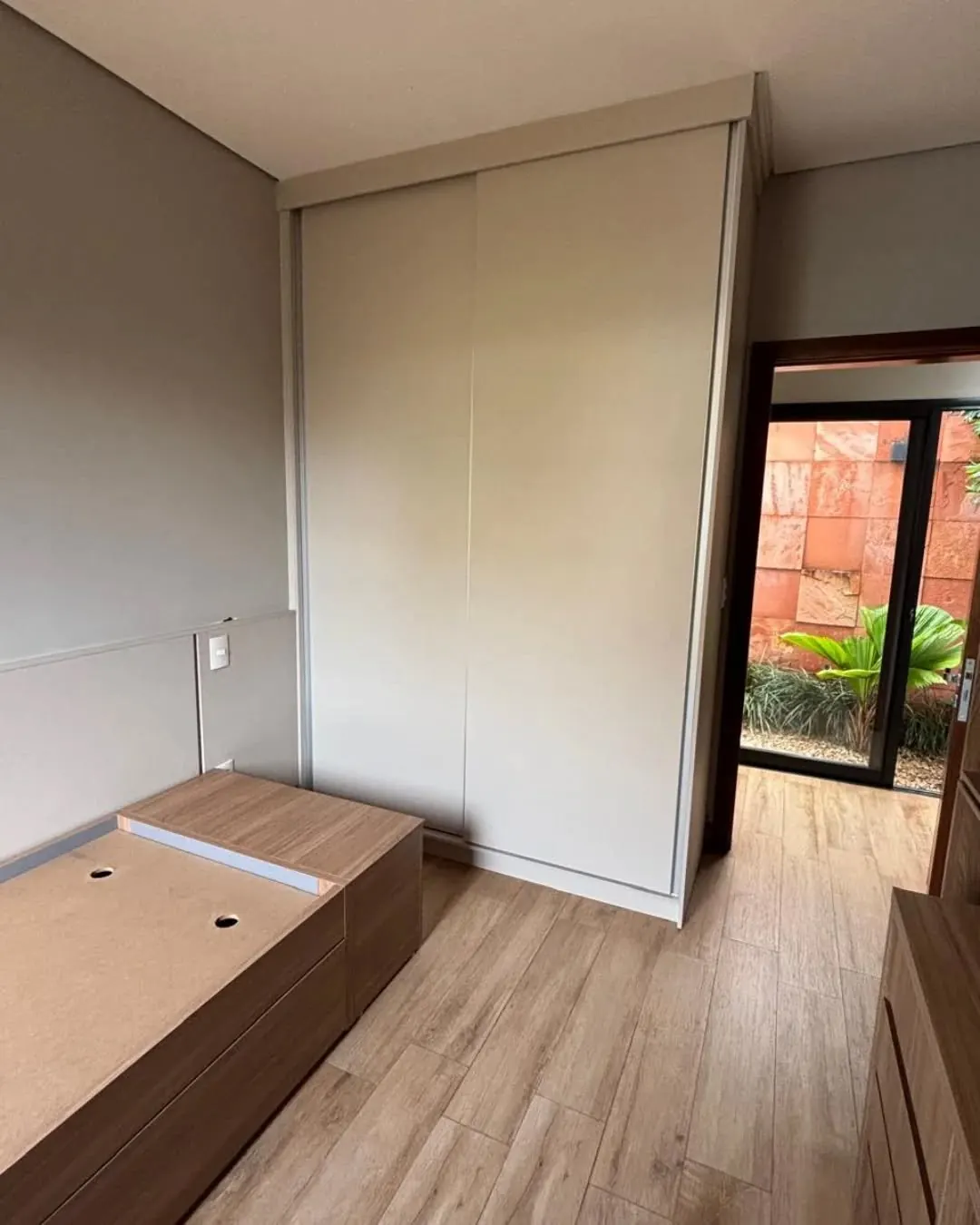 Quarto com guarda-roupa embutido de portas de correr e cama baú em madeira