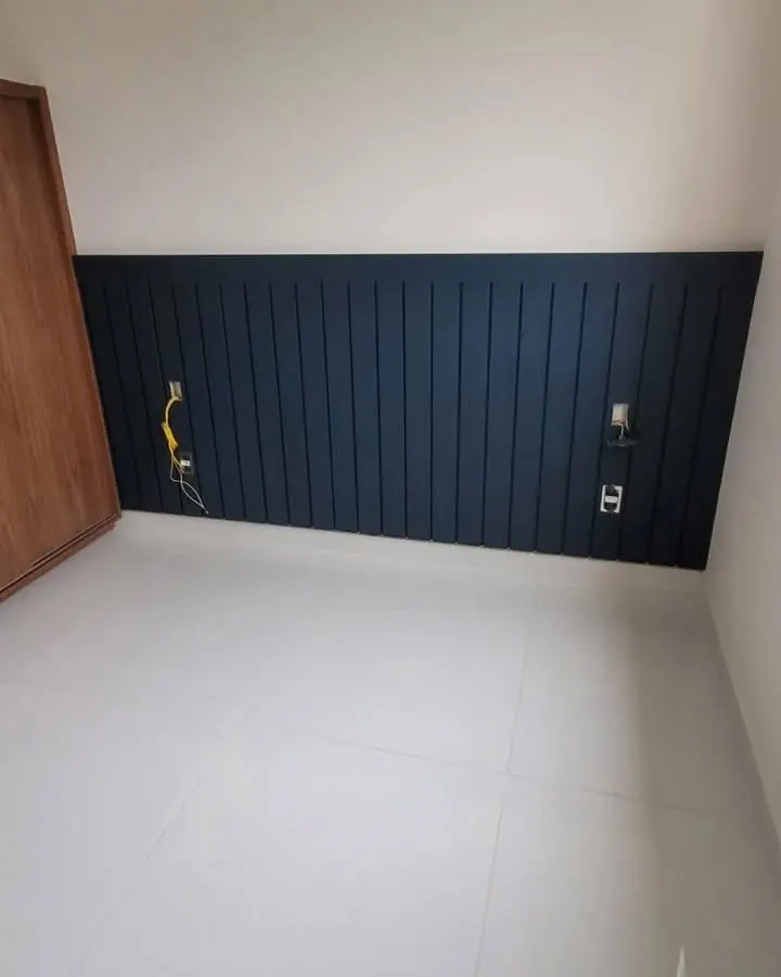 Painel de cabeceira ripado azul-marinho em quarto vazio, com armário em madeira ao lado