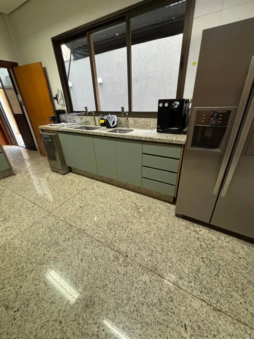 Bancada de cozinha verde-sálvia com pia sob janela, ao lado da geladeira